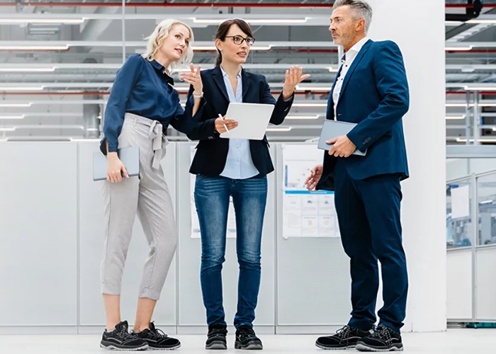 Three professionals discussing work holding tablet inside industrial office environment