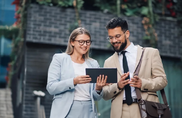 A profesionally-dressed lady in suit showing a tablet to another professional while standing outside
